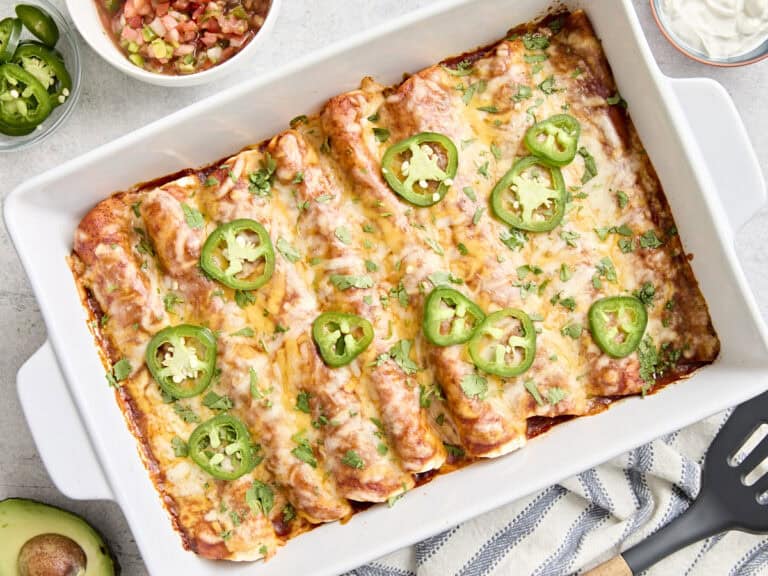 Overhead view of chicken enchiladas in a baking dish topped with fresh cilantro and sliced jalapenos.