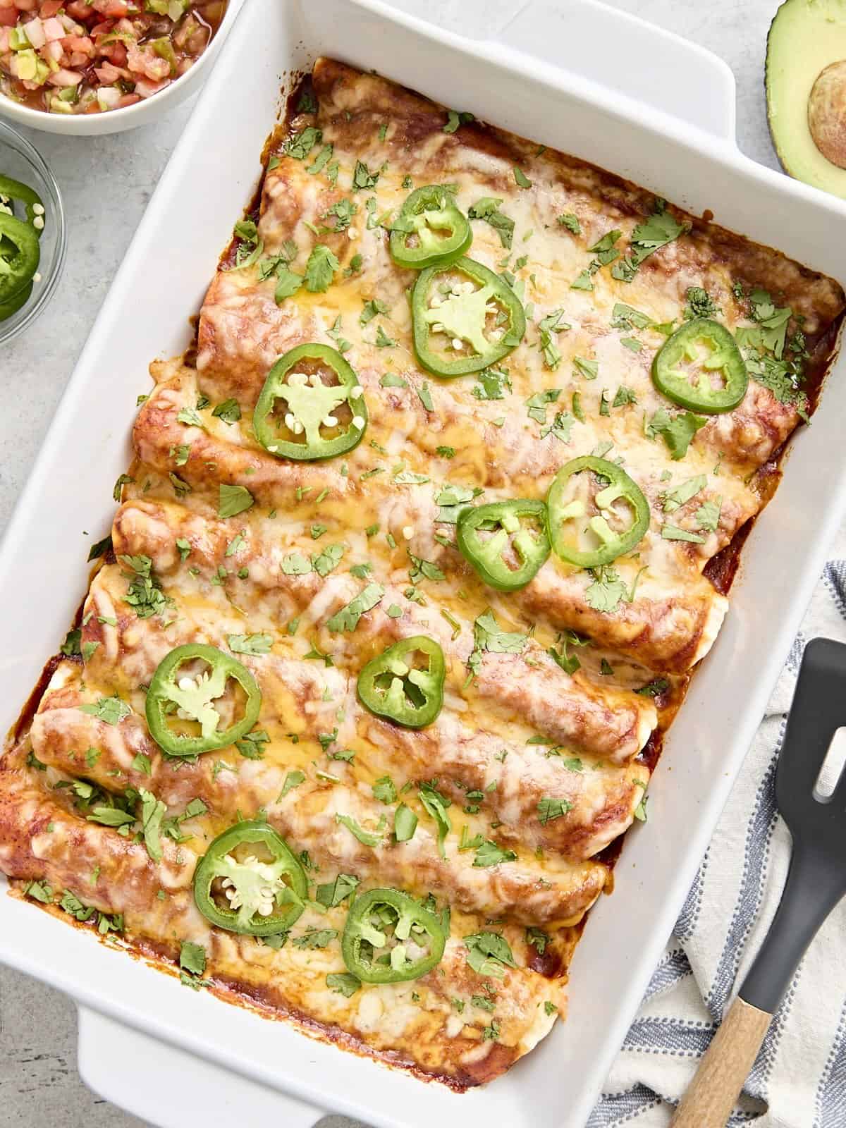 Overhead view of chicken enchiladas in a baking dish topped with fresh cilantro and sliced jalapenos.