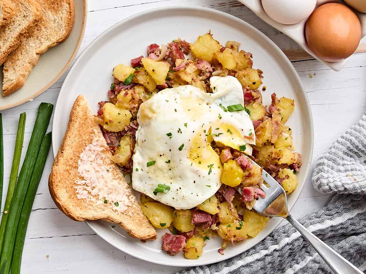 Overhead view of homemade corned beef hash on a plate with a slice of buttered toast and a fried egg.