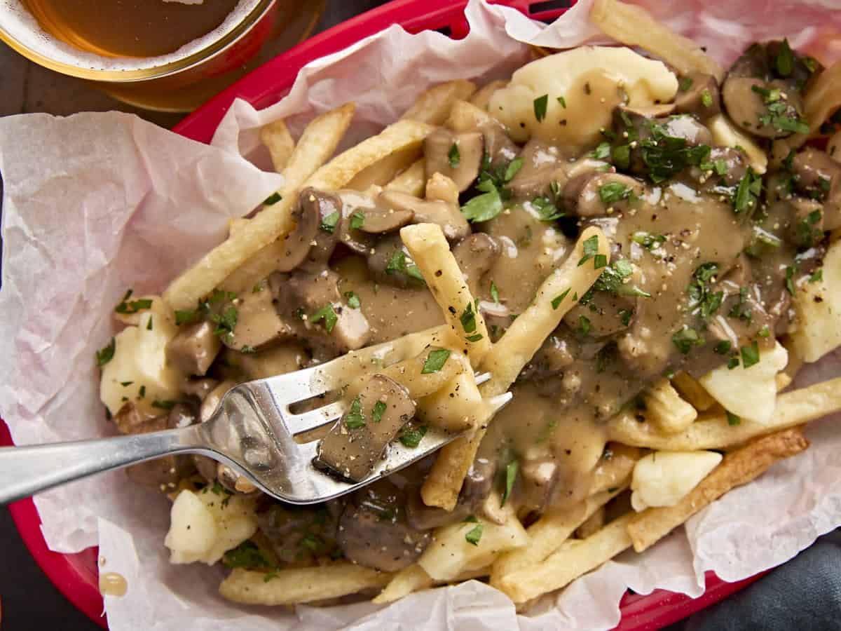 A fork taking some poutine from a red basket.