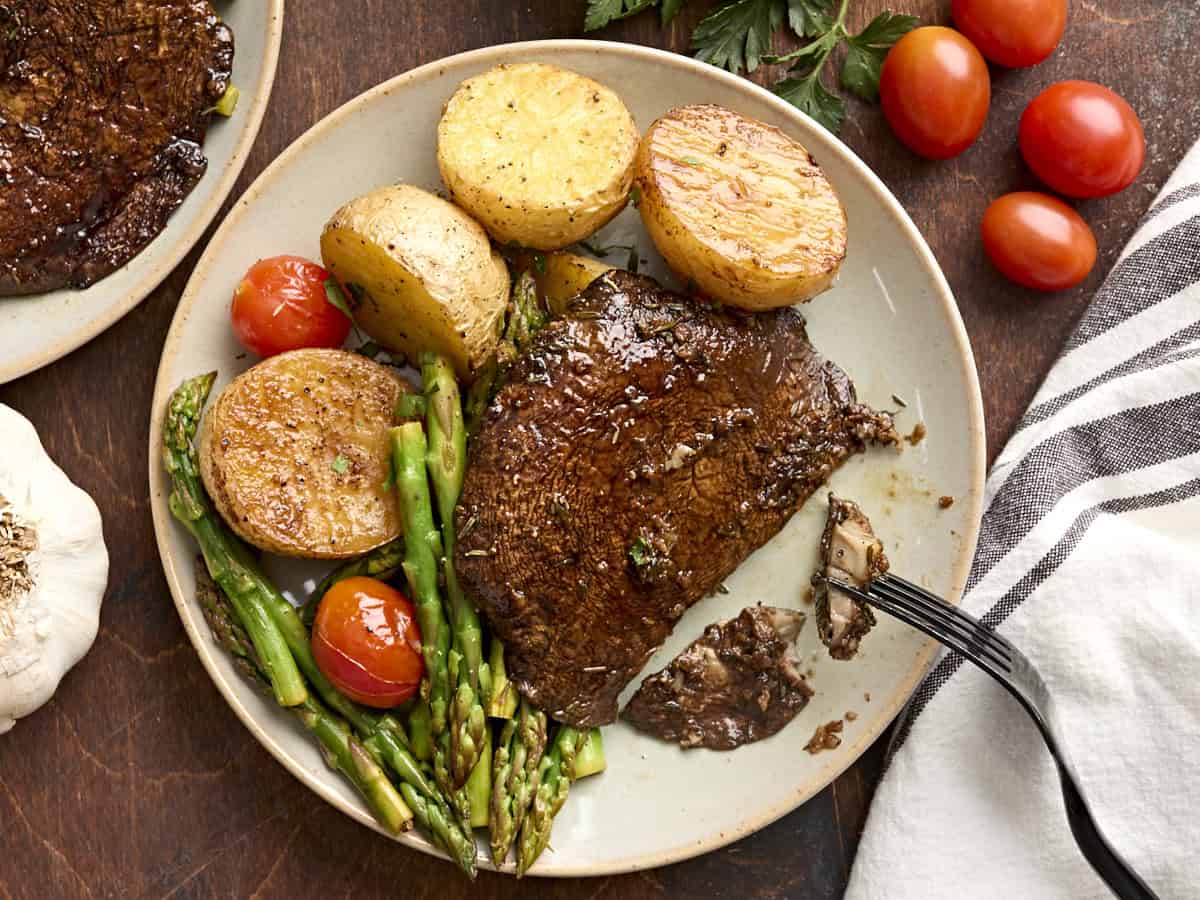 A mushroom steak dinner on a plate with a fork taking some of the mushroom.