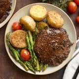 Overhead view of a mushroom steak dinner on a plate with asparagus, grape tomatoes, and potatoes.