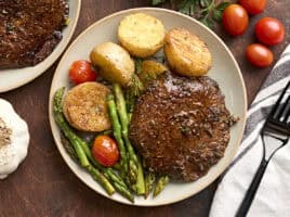 Overhead view of a mushroom steak dinner on a plate with asparagus, grape tomatoes, and potatoes.