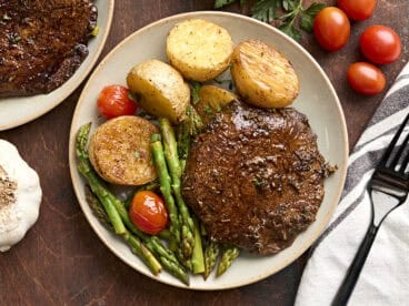 Overhead view of a mushroom steak dinner on a plate with asparagus, grape tomatoes, and potatoes.