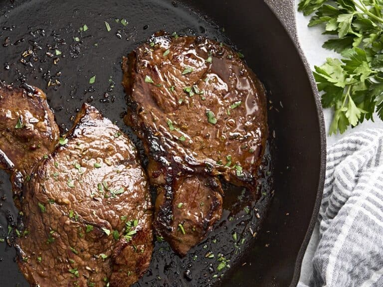 Overhead view of a marinated beef steak cooking in a cast iron skillet.