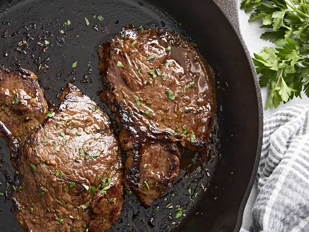 Overhead view of a marinated beef steak cooking in a cast iron skillet.