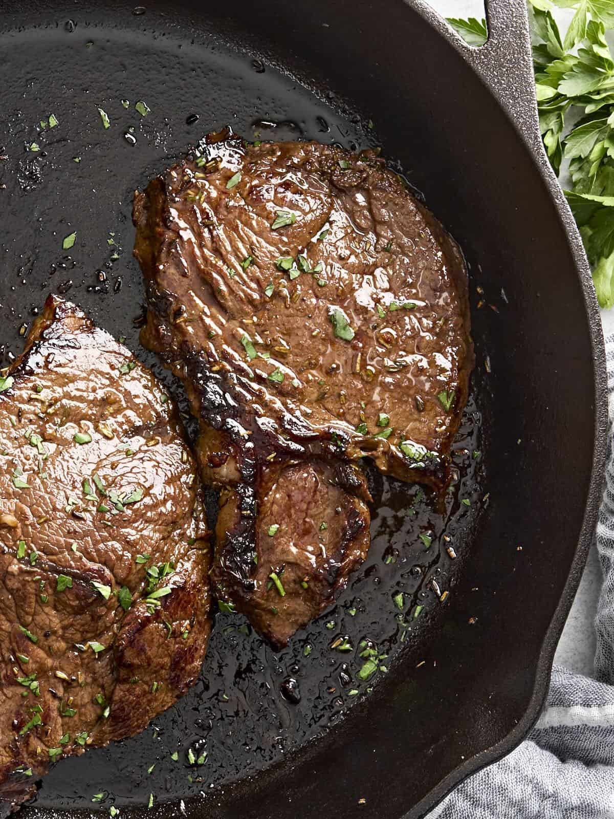 Overhead view of a marinated beef steak cooking in a cast iron skillet.