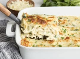 Side view of a slice of white chicken lasagna being lifted from a baking dish.