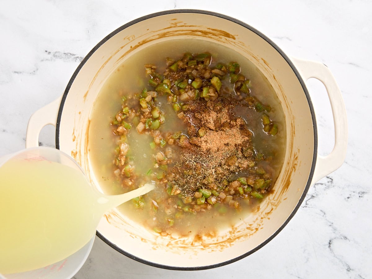 Chicken broth and seasonings added to a roux and diced veggies in a skillet.