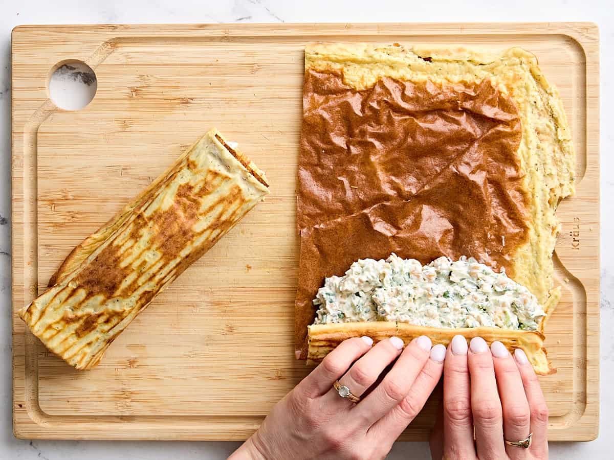 A hand rolling a cottage cheese wrap with filling.