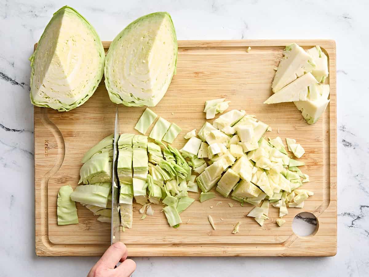 Cabbage being chopped up on a wooden cutting board.