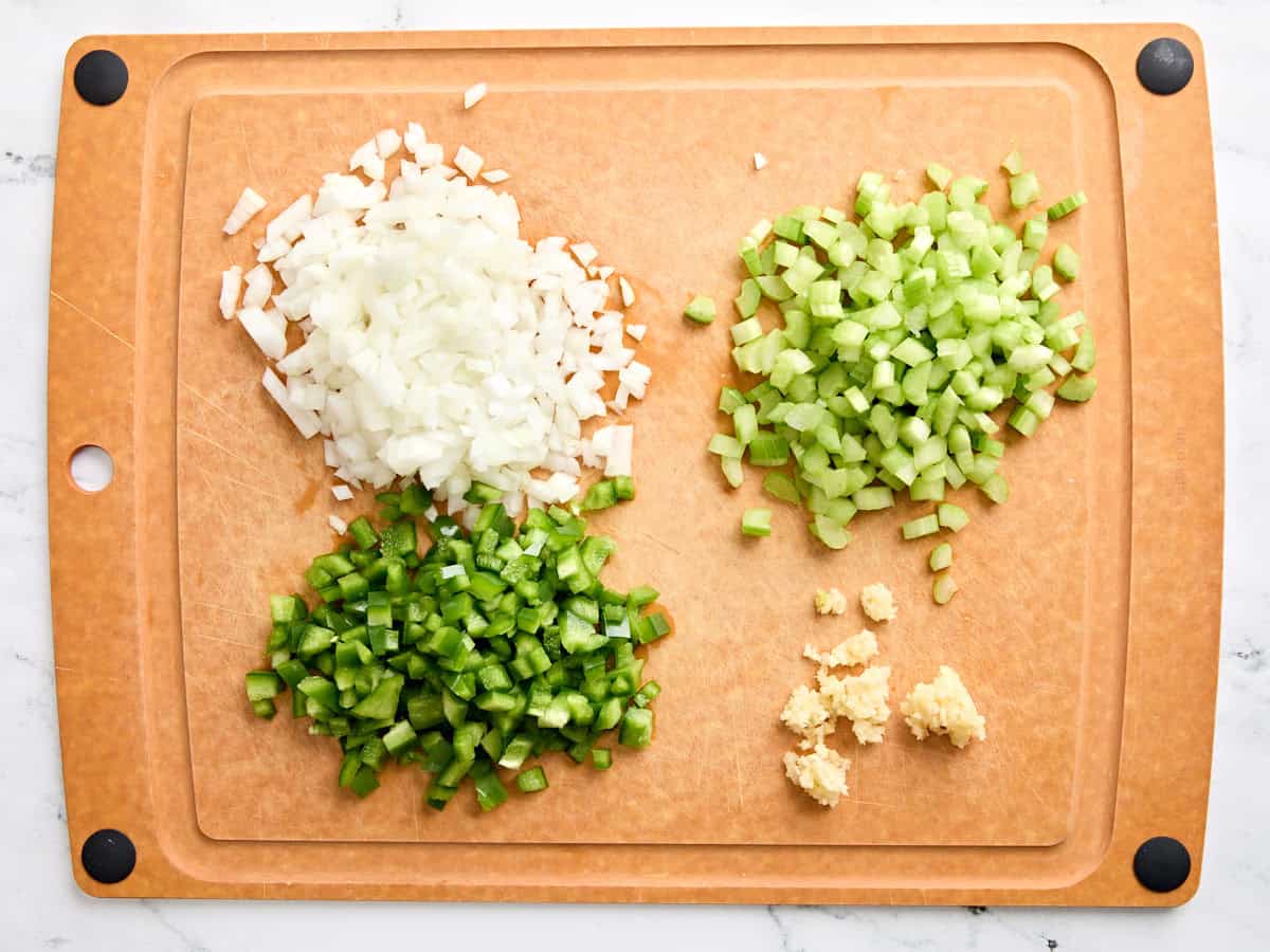 Diced onion, celery, green bell pepper, and minced garlic on a wooden cutting board.