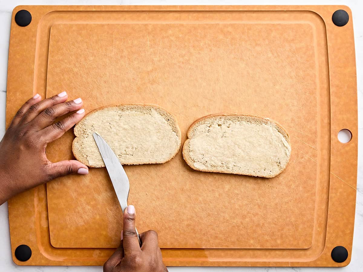 A knife buttering two pieces of rye bread.