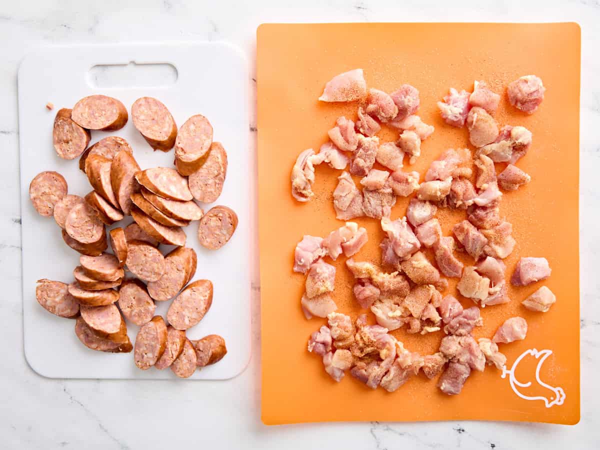 Sliced andouille sausage and diced chicken thigh on two cutting boards.