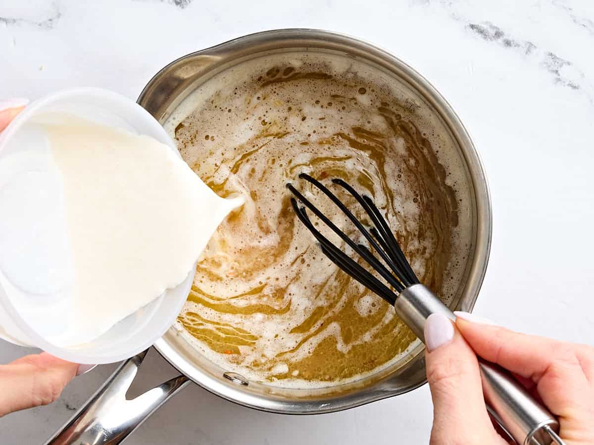 Heavy cream being whisked into melted butter in a sauce pan.