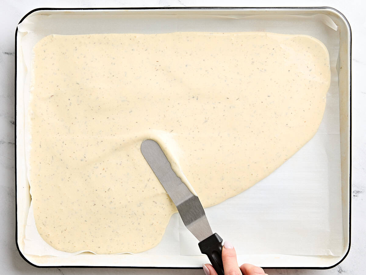 Cottage cheese and egg mixture being spread onto a parchment lined baking sheet.