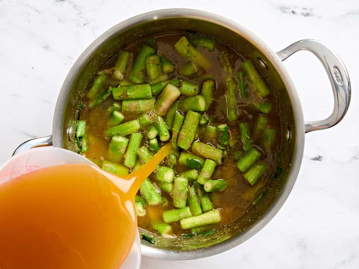 Vegetable broth added to sauteed asparagus in a sauce pot.