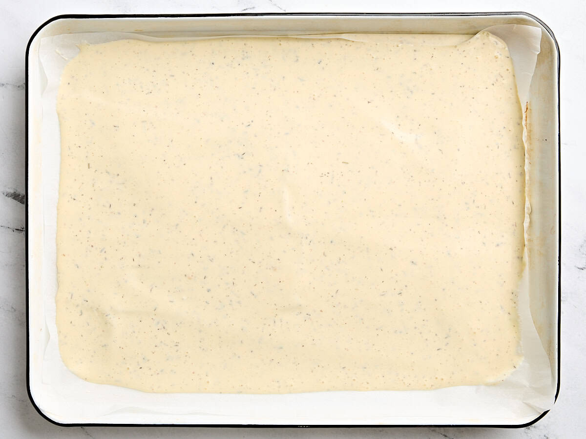 The batter for cottage cheese wraps fully spread onto a parchment lined baking sheet.