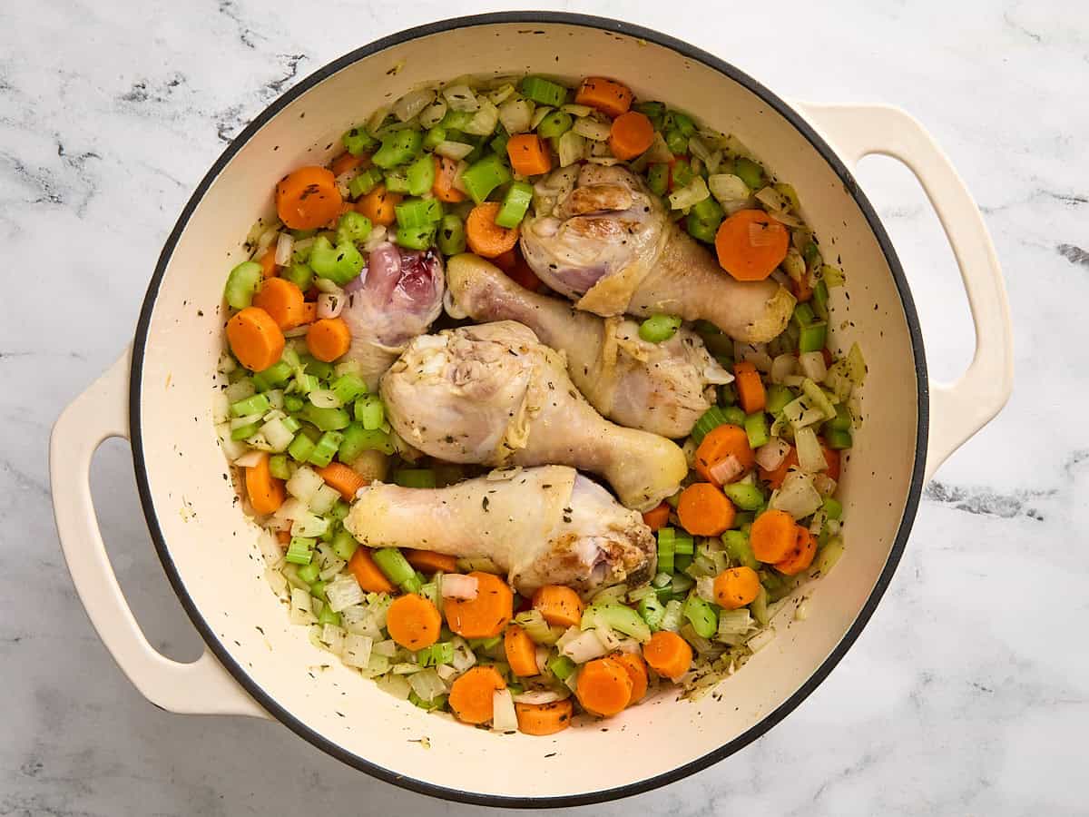 Browned chicken drumsticks in a stock pot with veggies.