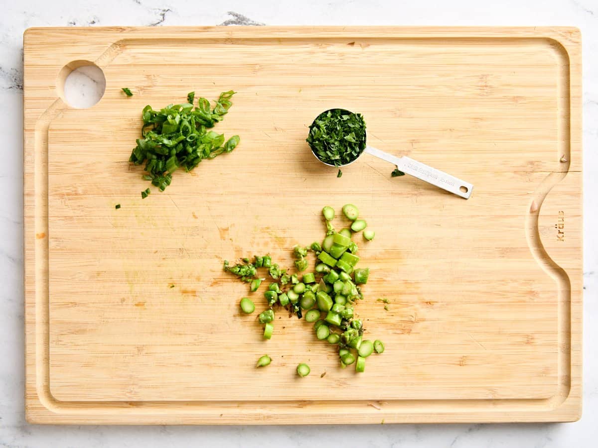 Diced cooked asparagus, sliced green onions, and minced parsley on a cutting board.