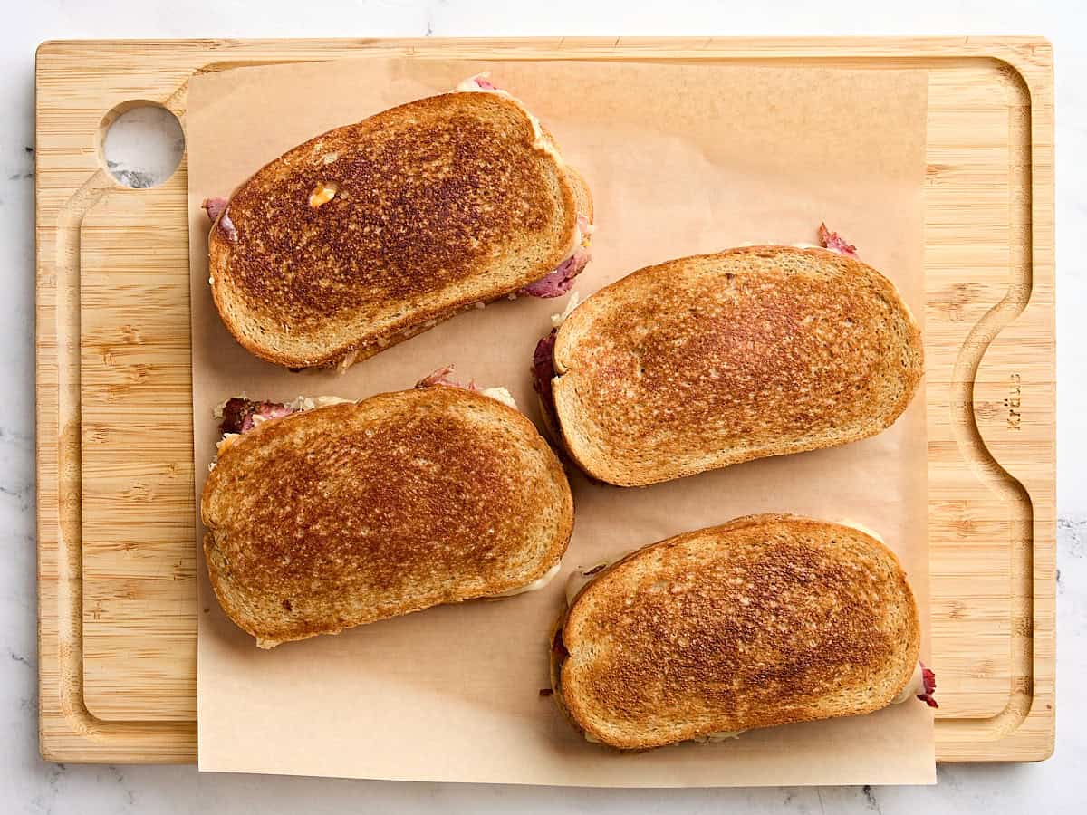 Four homemade Reuben Sandwiches on a cutting board.