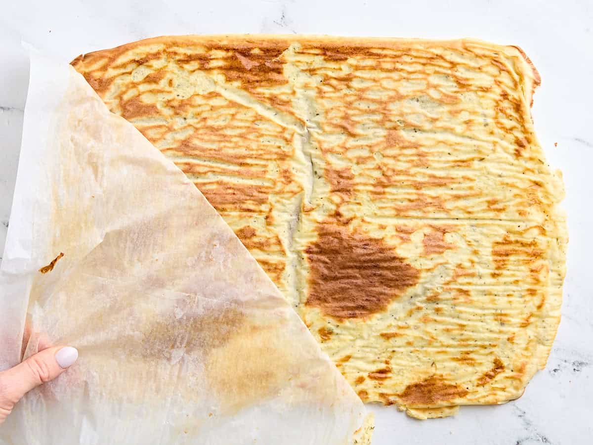 The parchment paper being pulled off a cooled baked cottage cheese and egg mix.