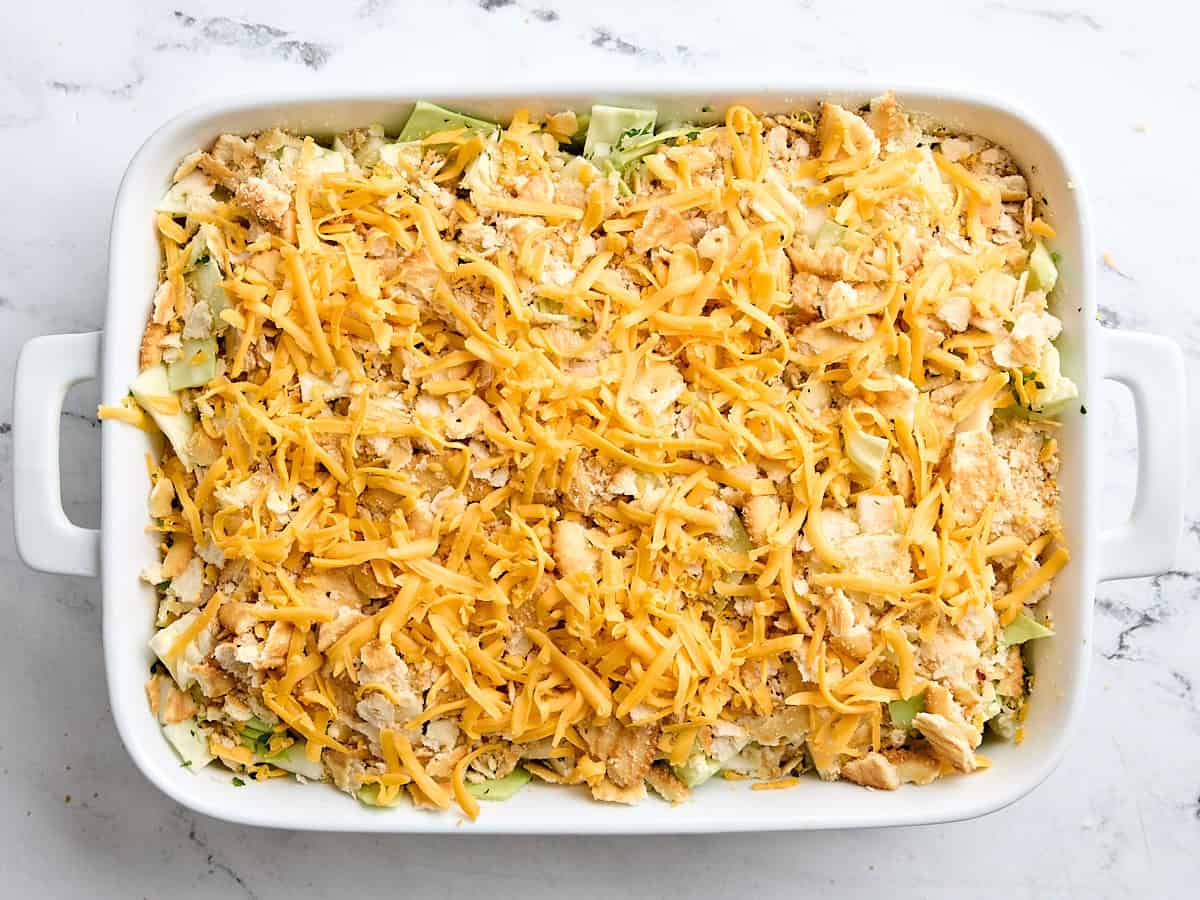 Shredded cheese added to a homemade cabbage casserole in a casserole dish.