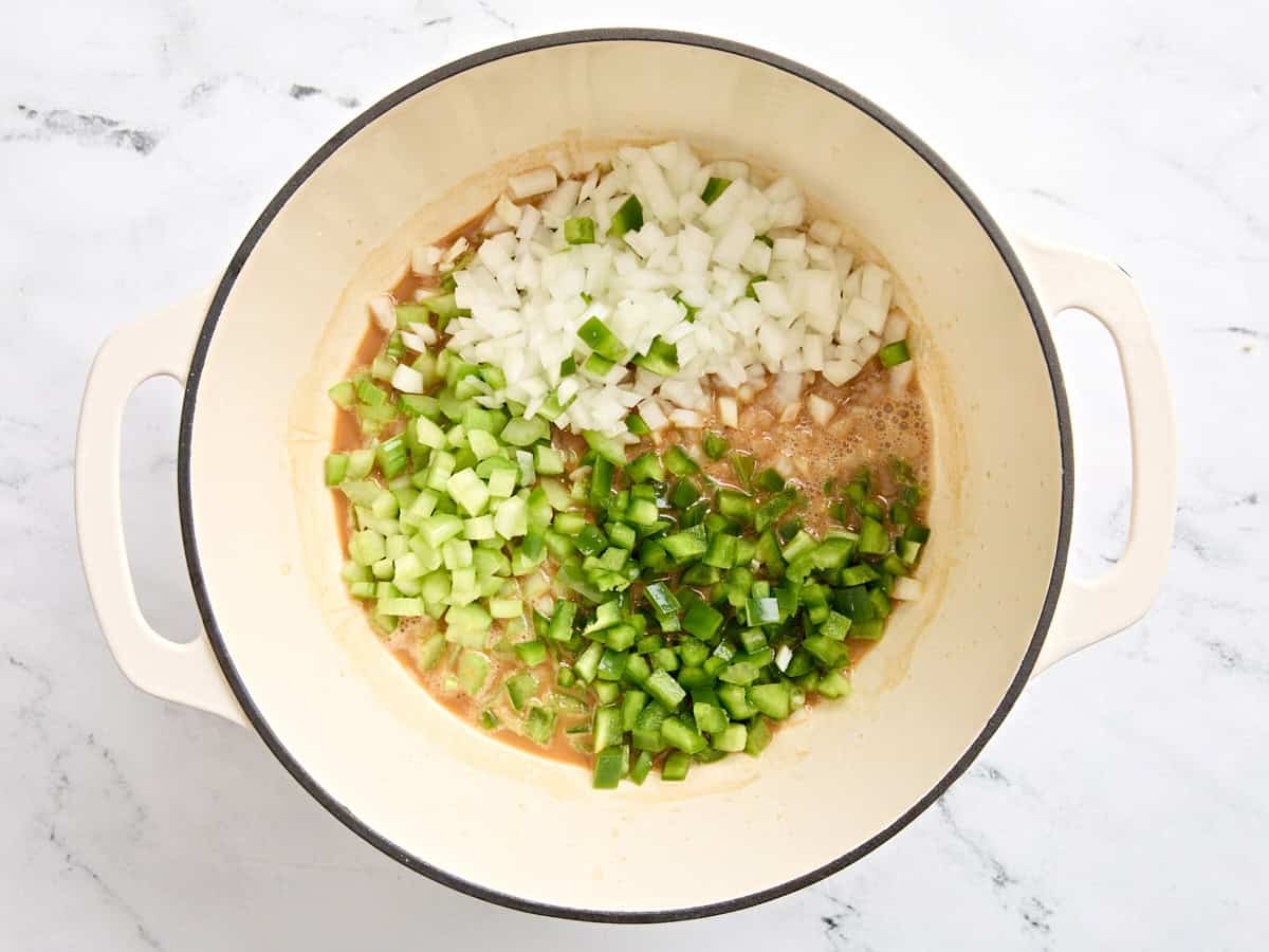 Diced onion, diced celery, and diced bell pepper added to a dark roux in a skillet.