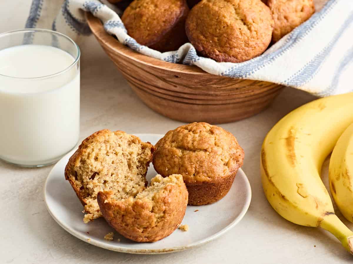 Two banana muffins on a plate with one broken in half.