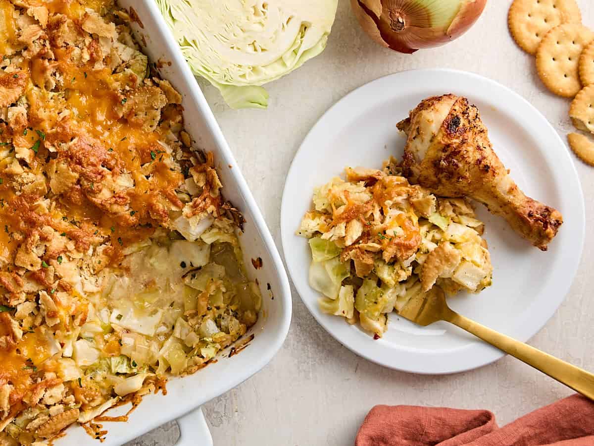 A plate with an air fried chicken leg and a side of cabbage casserole, next to a larger casserole dish.