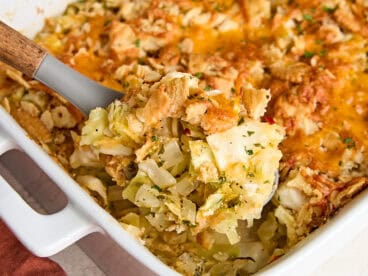 A serving spoon taking some cabbage casserole from a casserole dish.