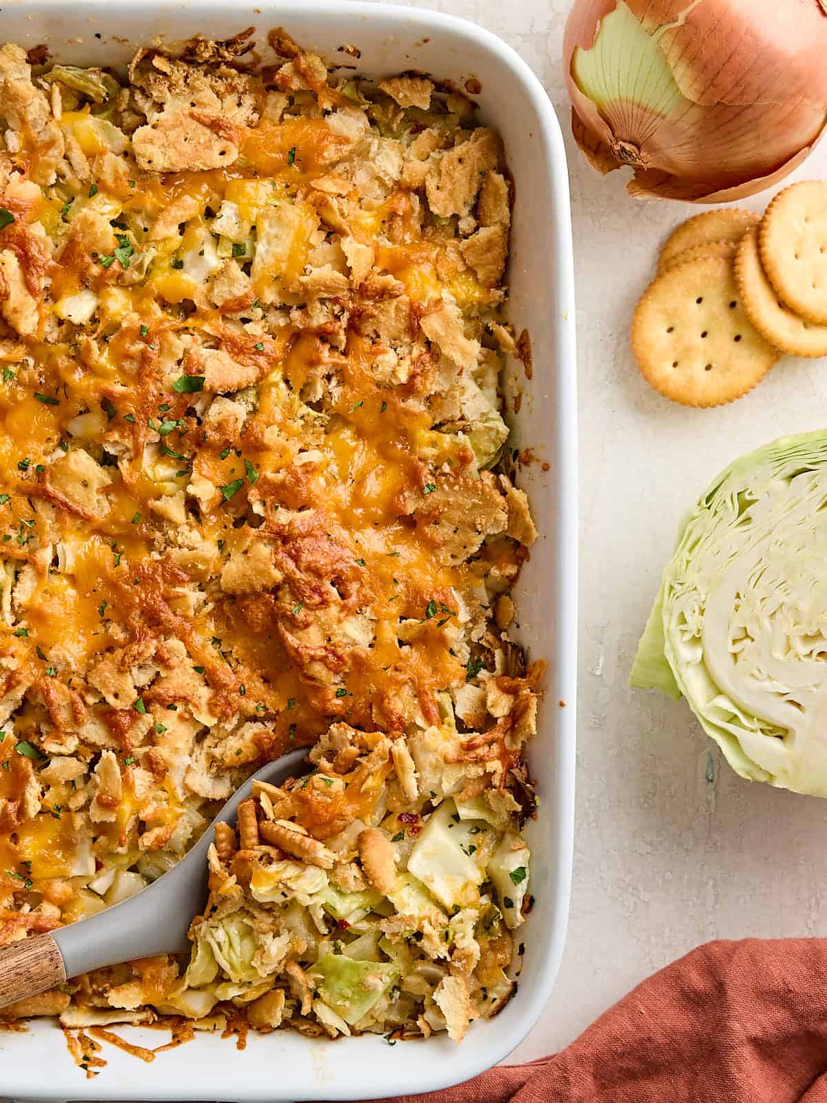 Overhead view of half a homemade cabbage casserole in a casserole dish with a serving spoon.