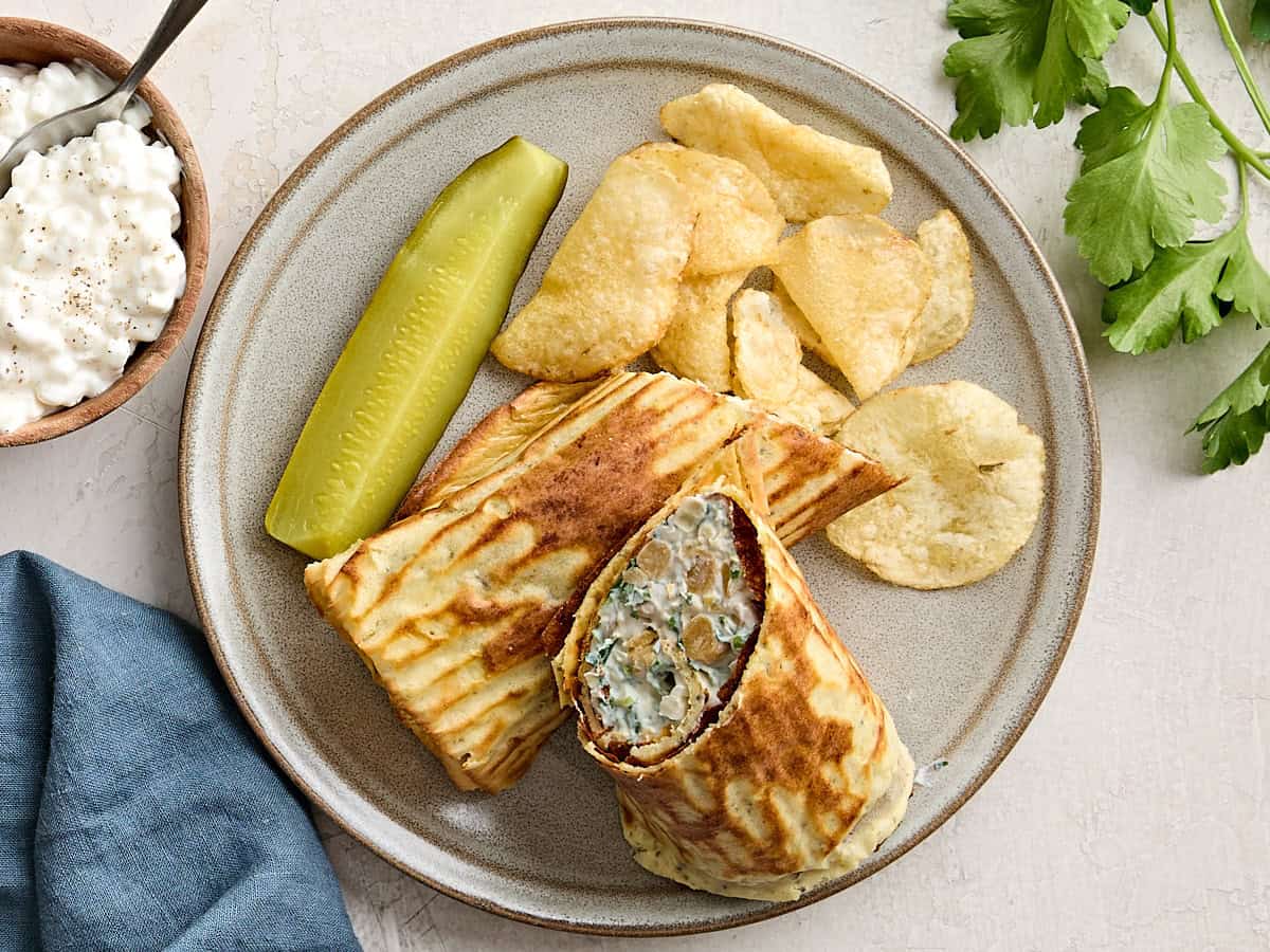 Overhead view of homemade cottage cheese wraps on a plate with potato chips and a pickle spear.