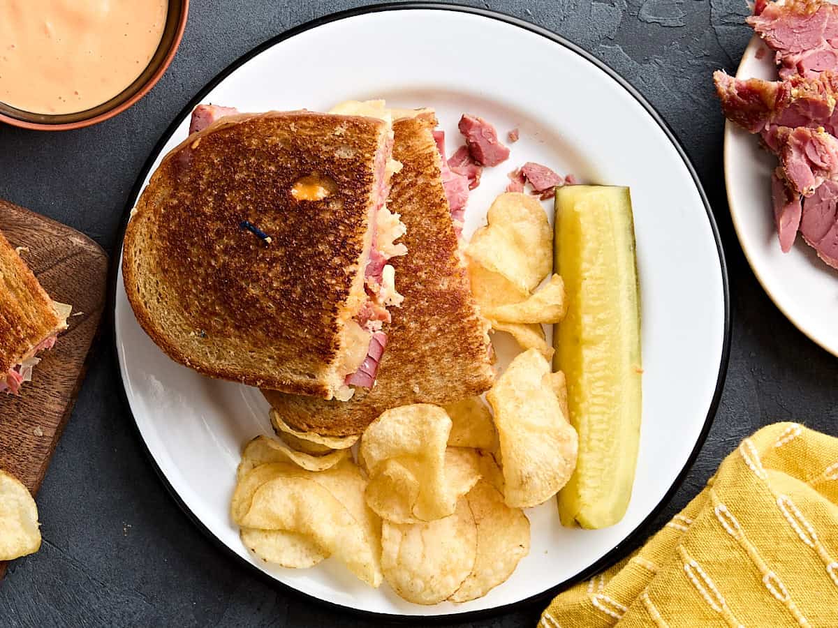 Overhead view of a homemade reuben sandwich on a plate with potato chips and a pickle spear.